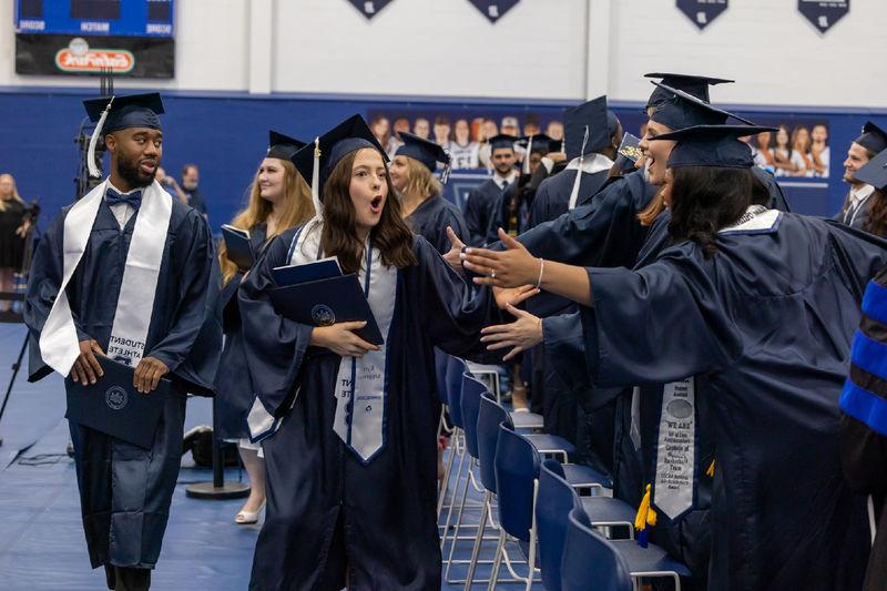 A graduate greets 2 friends as she exits after commencement. All are dressed in caps and gowns.