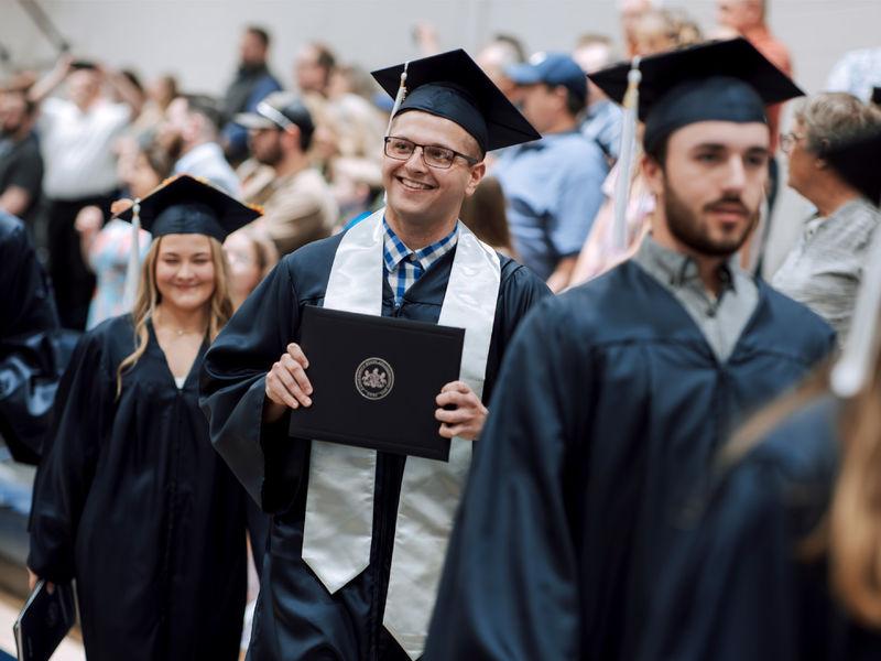 New Penn State graduate Kolton Lyons, who earned an associate degree in business administration, proudly displays his degree to onlooking family and friends during the commencement ceremony at Penn State DuBois.