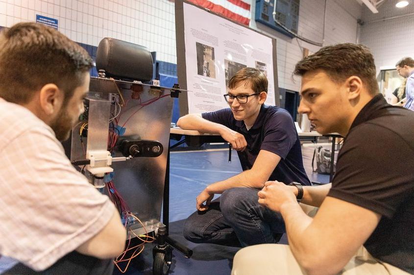 Three male 学生s look at autonomous wheelchair